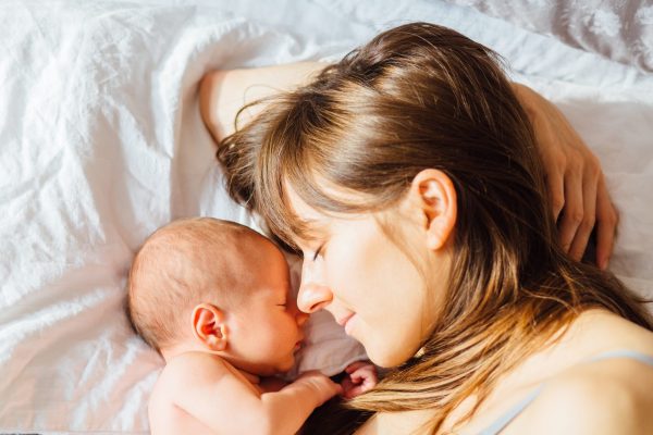 Mother with newborn baby sleeping on the bed at home. Top view, close up.